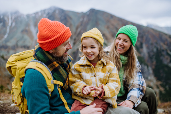 Happy family resting, having snack and enjoying the view during hiking together in an autumn mountains. Mom, dad and daughter on kid friendly hike.