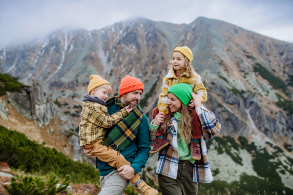 Happy parents with their little kids on piggyback at an autumn hike, in the middle of mountains. Concept of healthy lifestyle.
