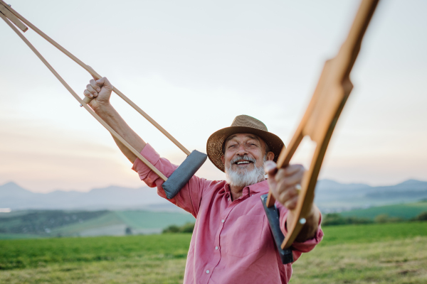 Senior man holding crutches in the air, he is happy about his recovery. Recovery, rehabilitation after injury or surgery in the nature. Concept of recovery and physical therapy