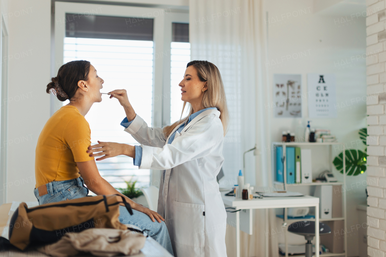 Doctor examining young patient's sore throat, looking into the throat using a tongue depressor.