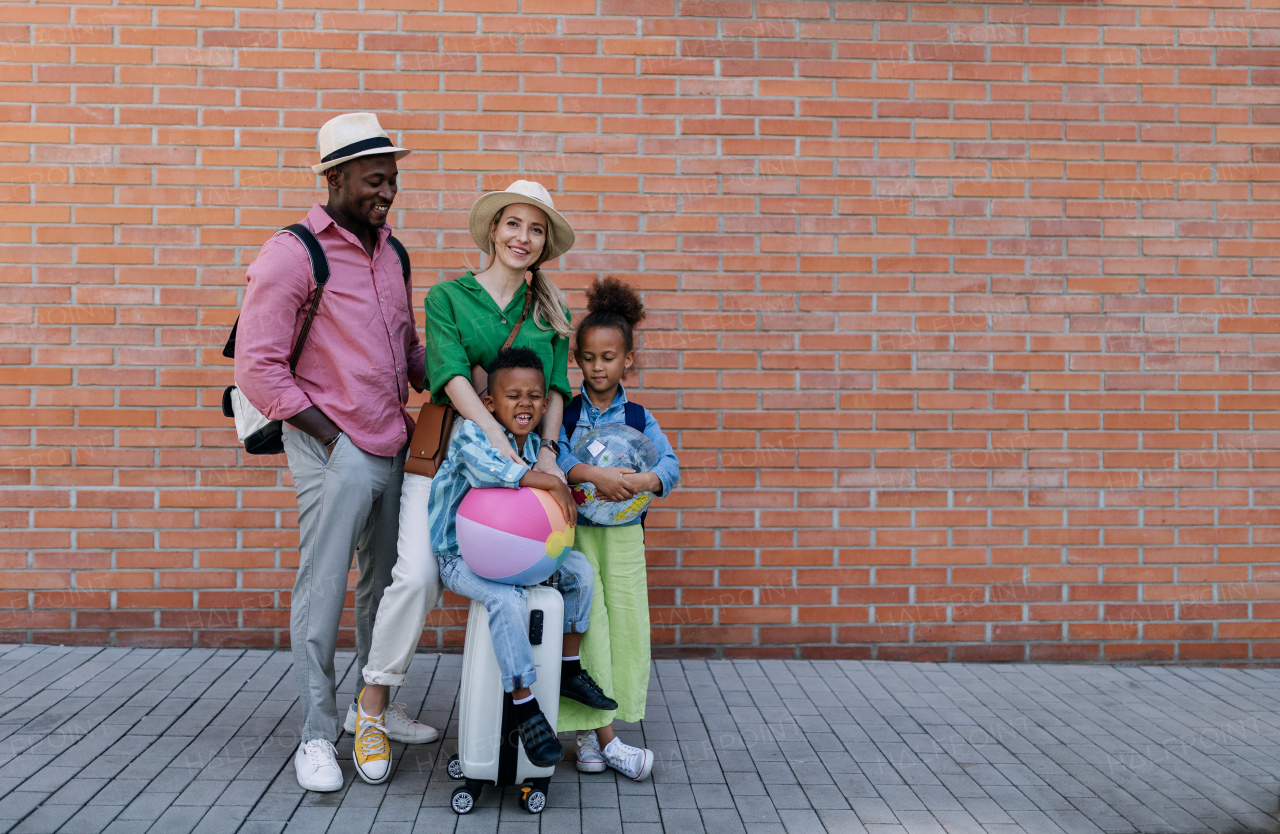 Multiracial family travelling together with small kids. Posing in front of a brick wall.