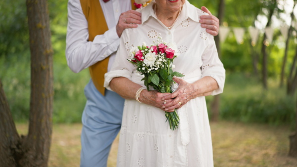 Mid section of senior hands with wedding bouquet and golden wedding rings during their marriage.