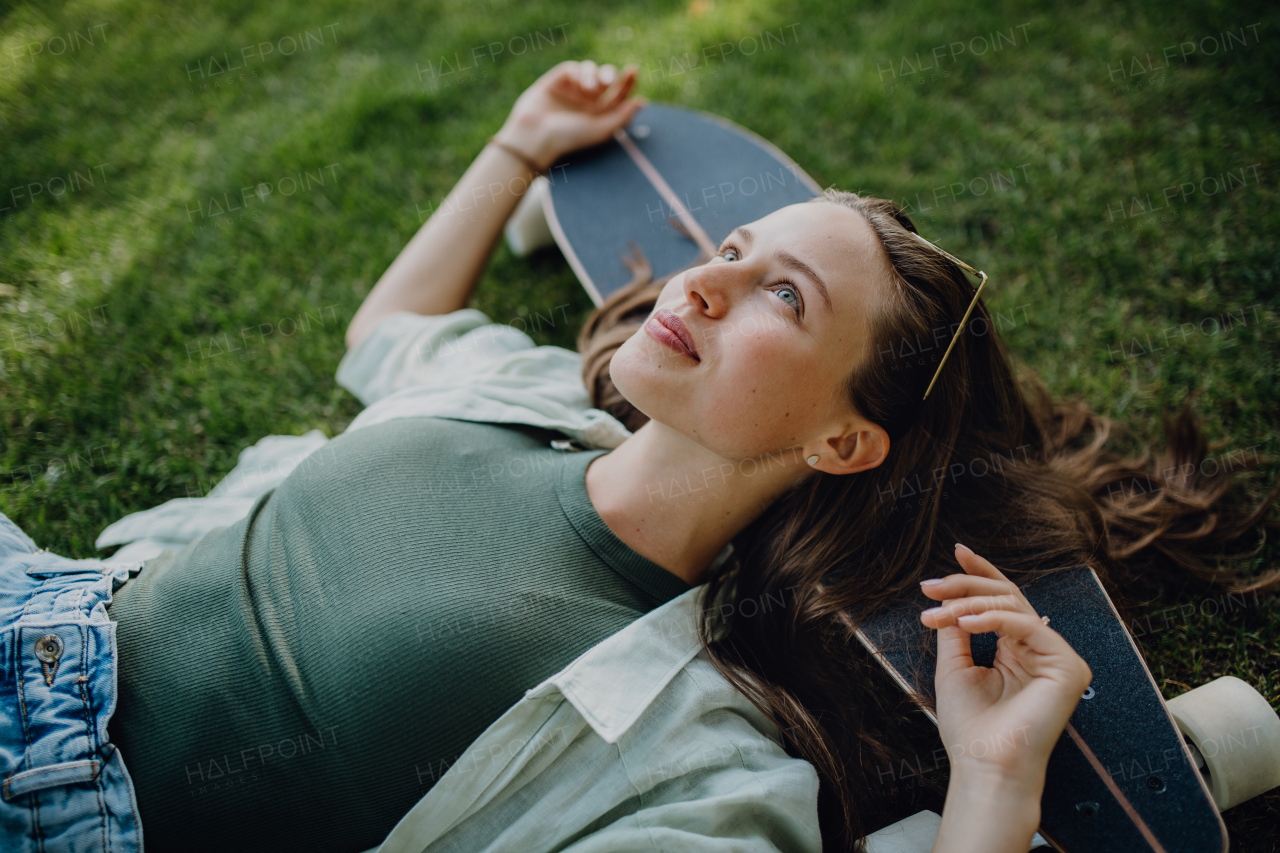 High angle view of young woman lying on the grass with a skateboard.