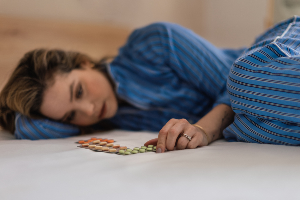 Young woman with depression lying in bed, looking at the pills.
