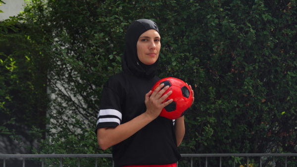 Beautiful female football player in hijab with a ball in her hand. The woman plays soccer for relaxation. Concept of muslim woman in sport.