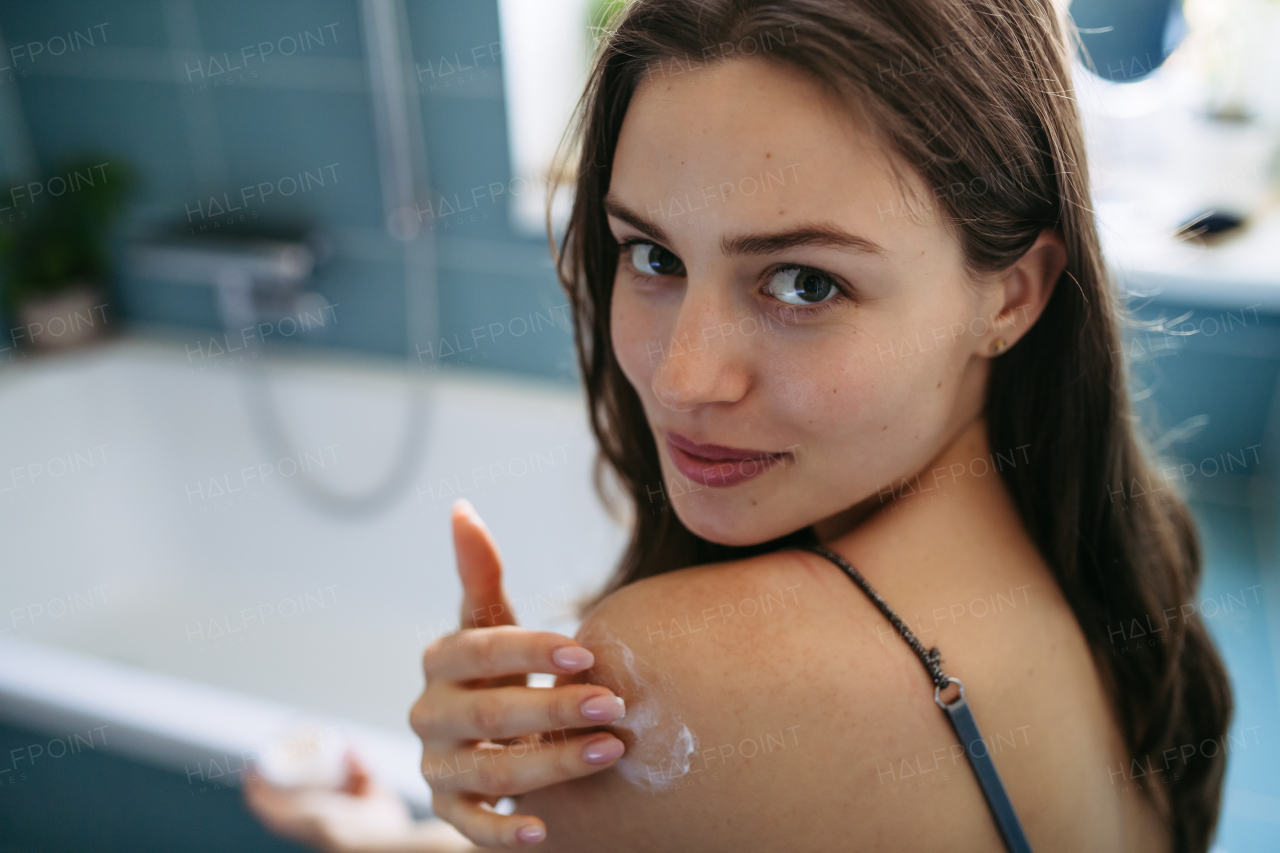Young woman applying sunscreen before being in sun, looking at camera. Skincare, body care routine.