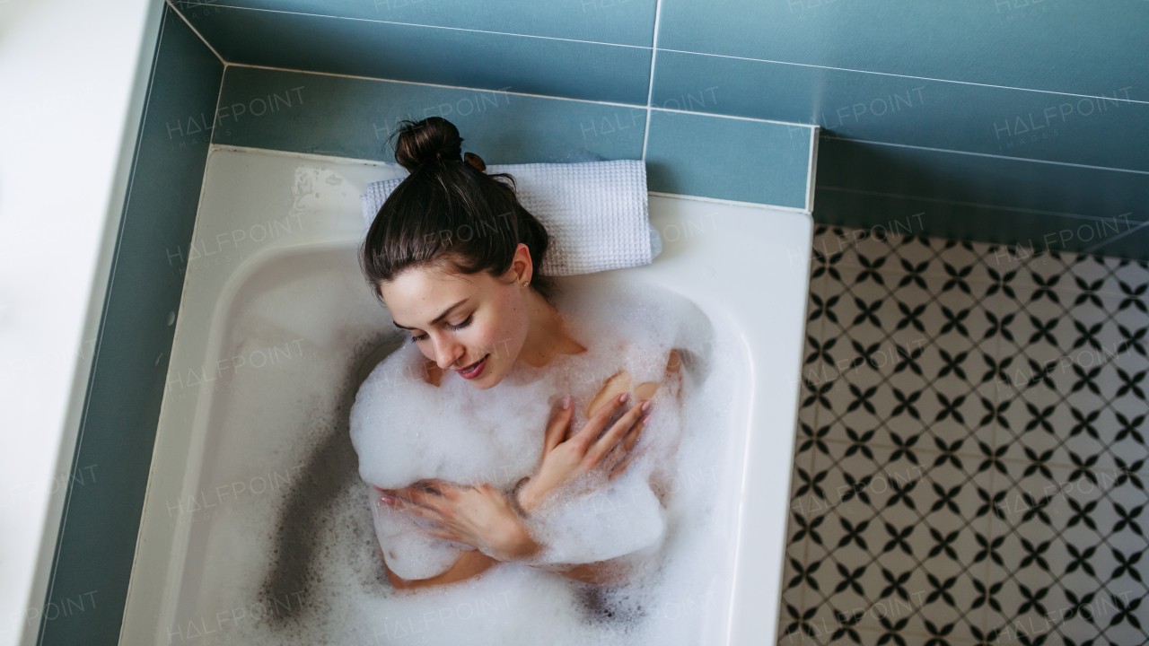 Top view of beautiful woman relaxing in warm bathwater, soaking in bathtub. Enjoying bubble bath and smiling.