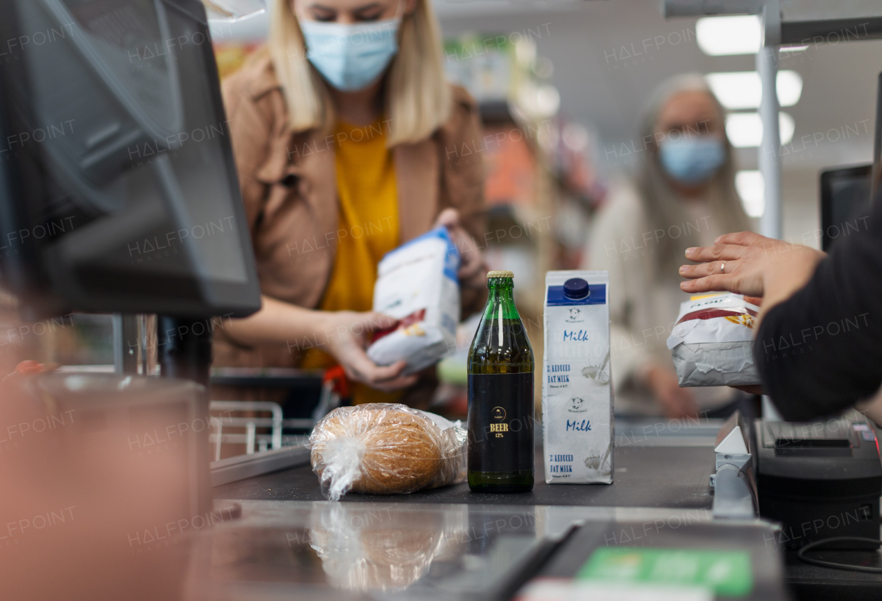 A young woman shopping in supermarket, putting products on checking desk during pandemic