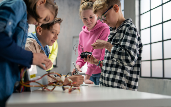 A group of happy kids with their science teacher and electric toys, robots at robotics classroom