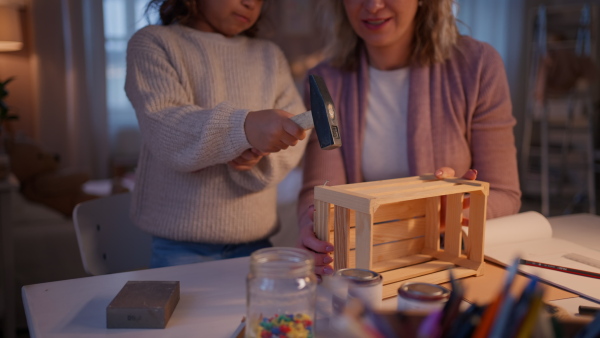 A happy little girl renovating a wooden crate together with her mother at home.