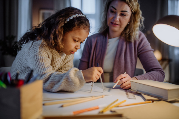 A mother helping her daughter with homework, drawing a circle with comasses in evening at home.