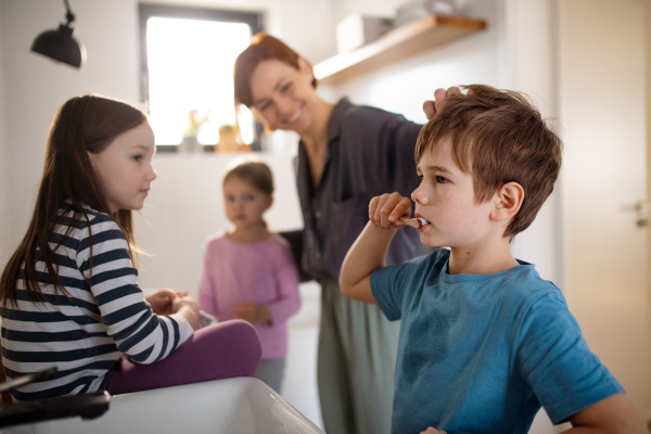 A mother with three little children in bathroom, brushing teeth.