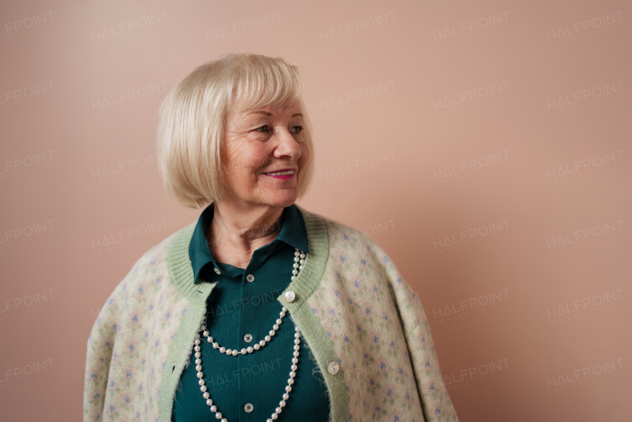 A smiling elegant elderly woman on pink color background, studio portrait