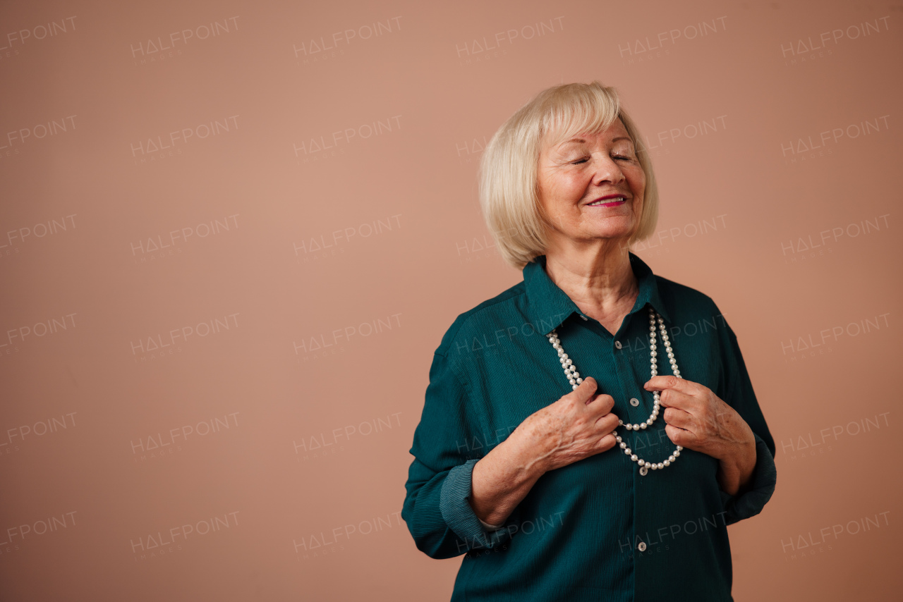 A smiling elegant elderly woman with pearls on pink color background, studio portrait