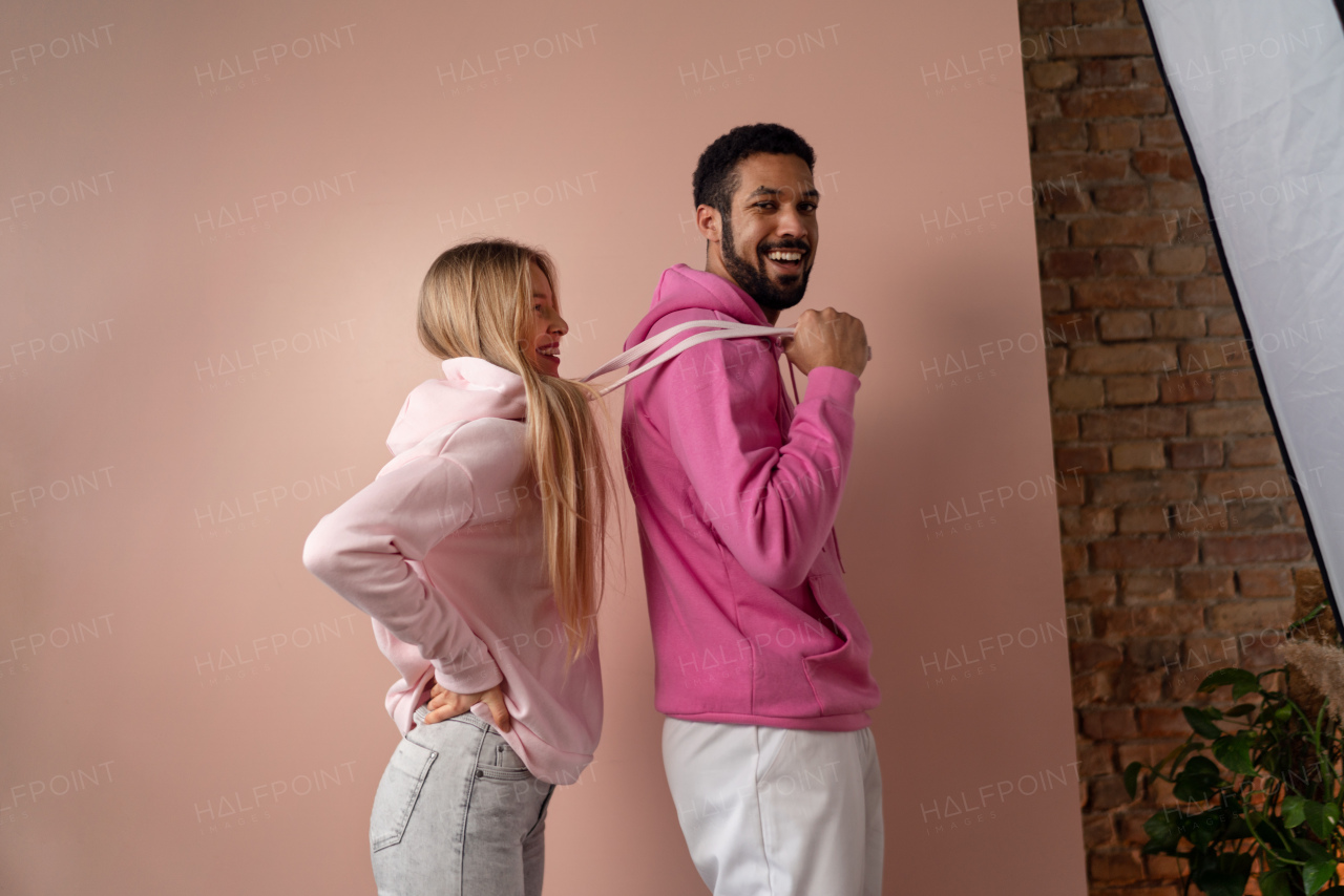 A fashion studio portrait of a happy young blonde woman in hoodie posing over pink background.