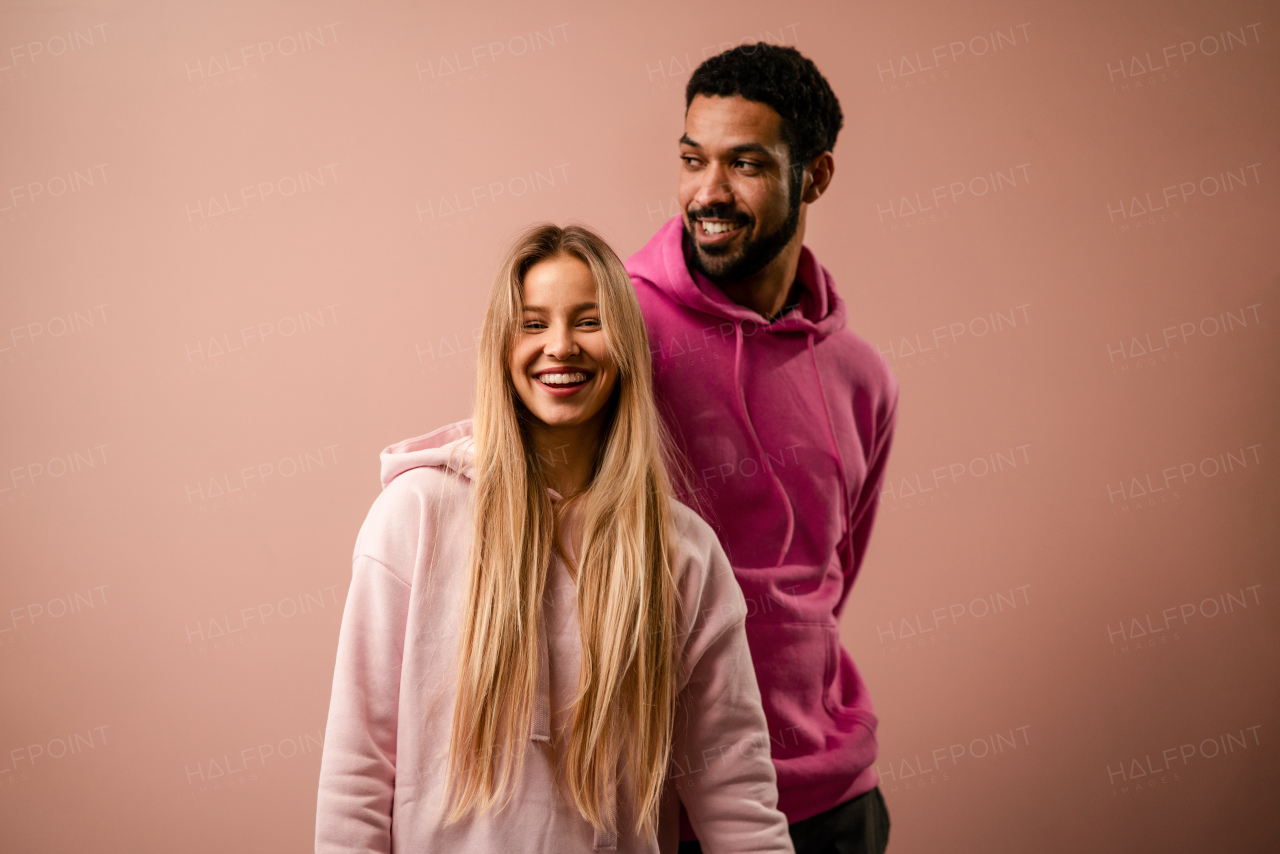 A fashion studio portrait of a happy young blonde woman in hoodie posing over pink background.