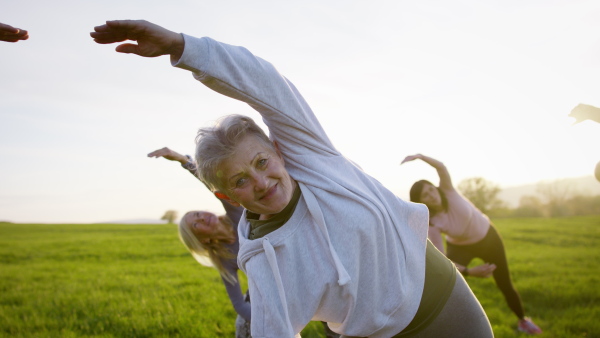 A group of seniors with sport instructor doing exercise outdoors in nature, active lifestyle.