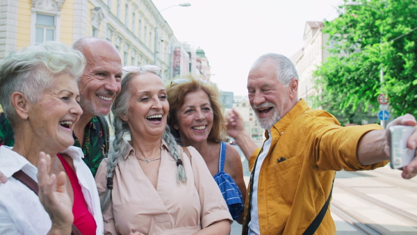 A group of happy senior friends tourists on a walk in city, taking selfie.