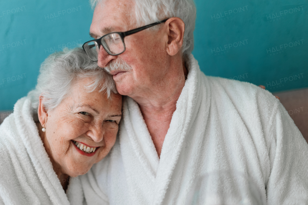 Portrait of happy senior couple sitting together in the bathrobe on sofa, having nice time at home.