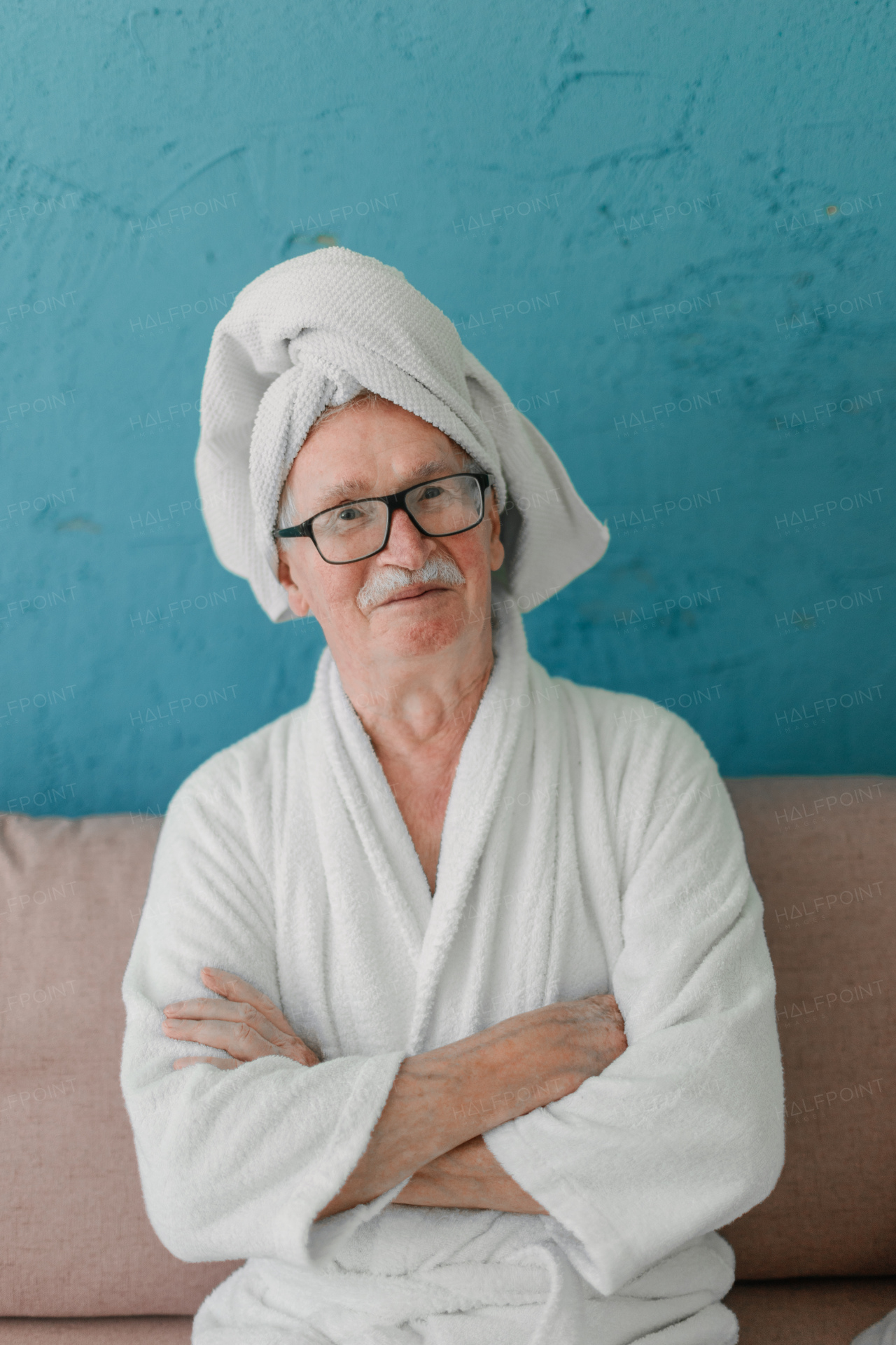 Happy senior man in glasses sitting at sofa in bathrobes and looking at camera.