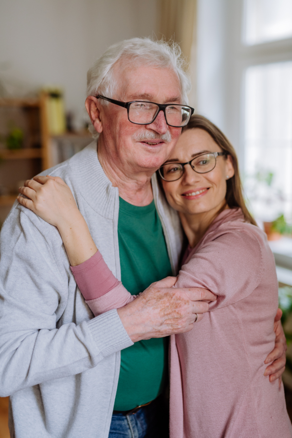 An adult daughter hugging her senior father when visitng him at home.