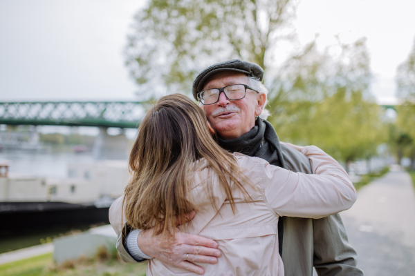 A rear view of adult daughter hugging her senior father when meeting him outdoors in street.