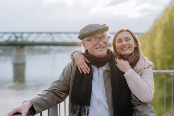 An adult daughter hugging her senior father outdoors in park on spring day.