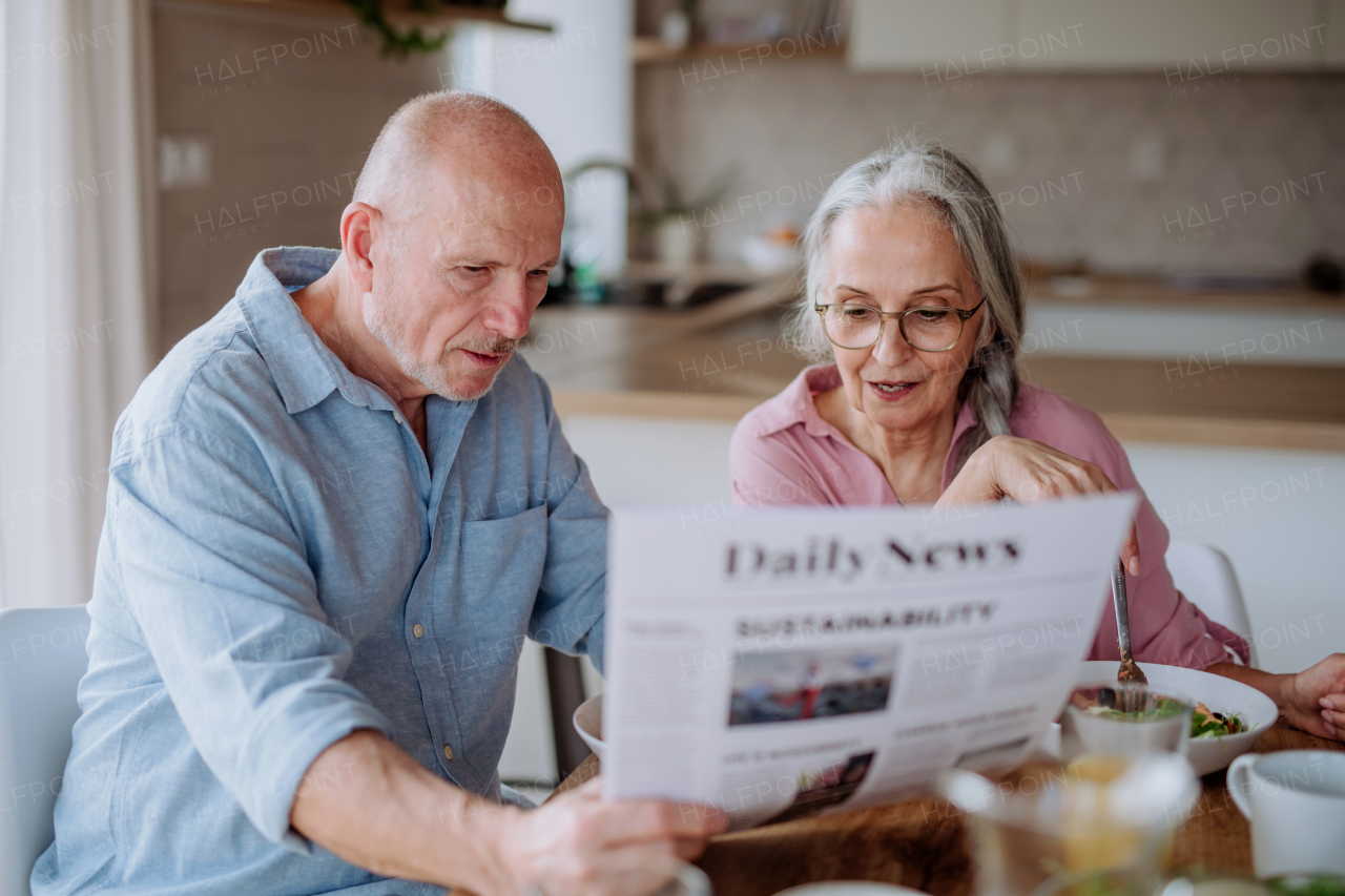 A happy senior couple having breakfast and reading newspaper together at home.