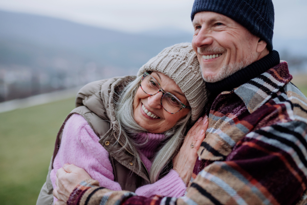 A senior man hugging and consoling his wife outdoors in garden in winter.
