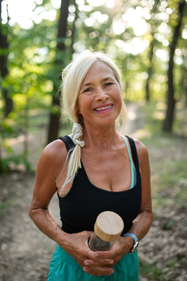 A portrait of active senior woman runnerwith water bottle outdoors in forest.