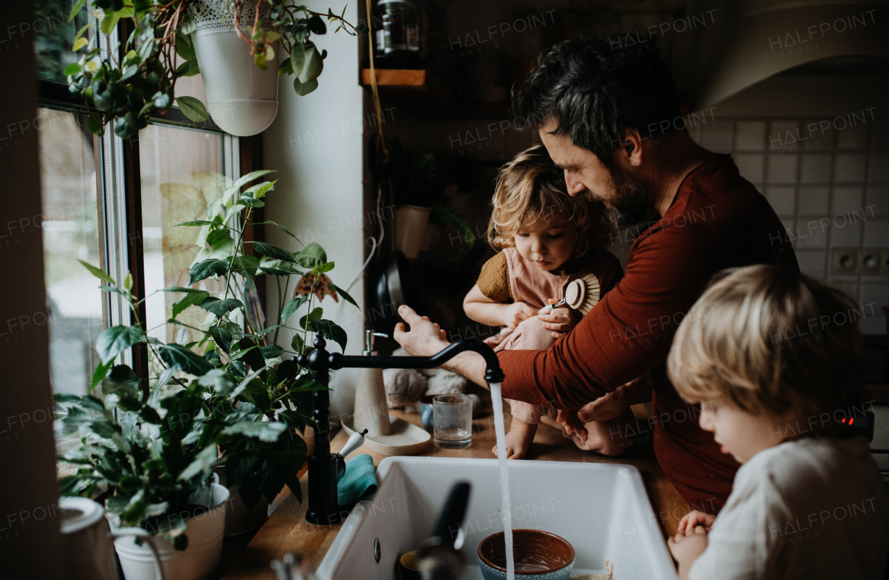 A mature father with two small children washing dishes indoors at home, daily chores concept.