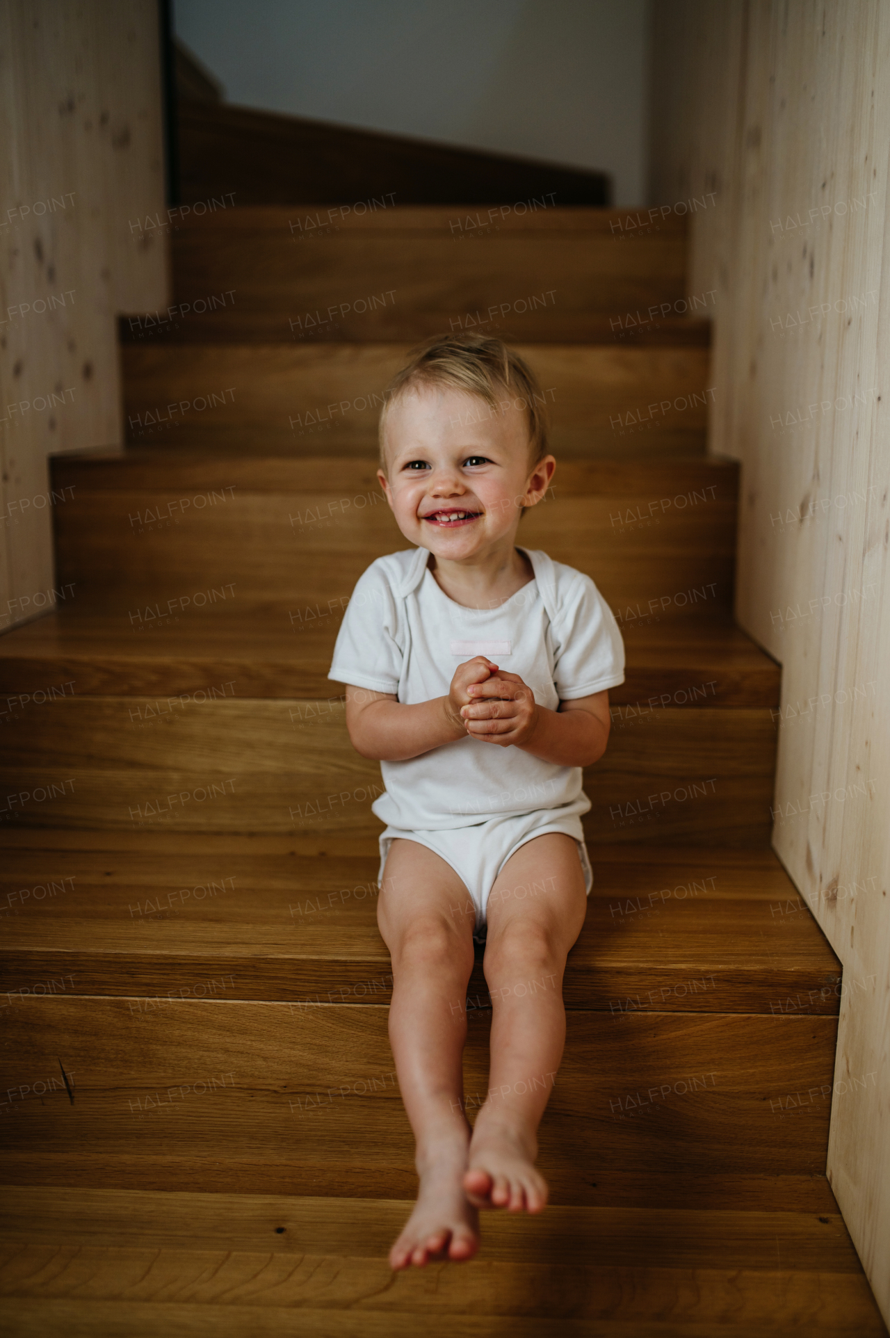 A cute little girl sitting on stairs at home and looking at camera.