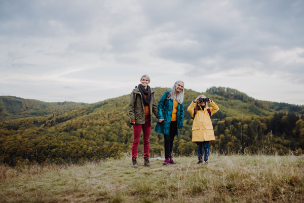 A small girl with mother and grandmother hiking outoors in autumn nature.