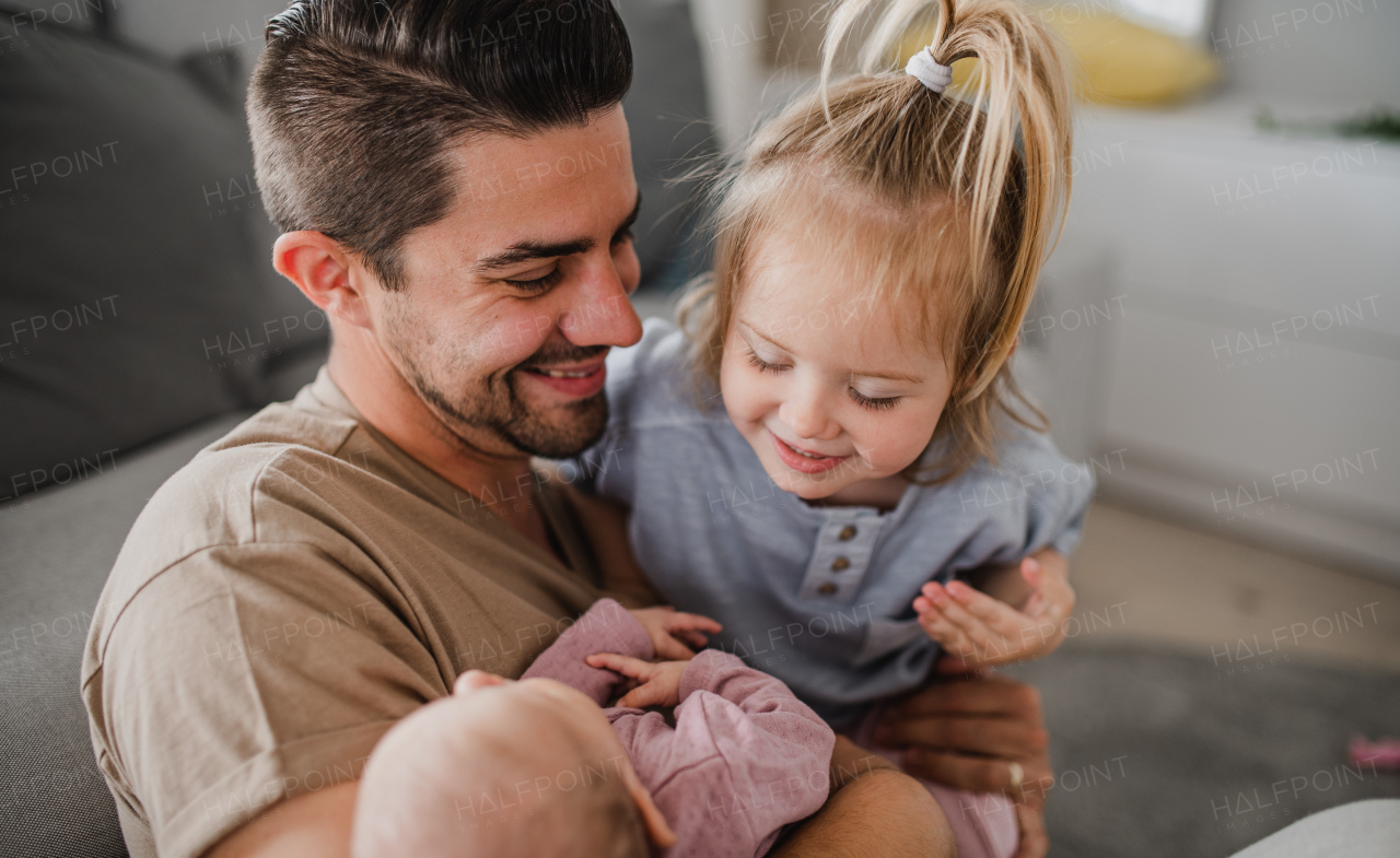 A happy young man taking care of his newborn baby and little daughter indoors at home, paternity leave.