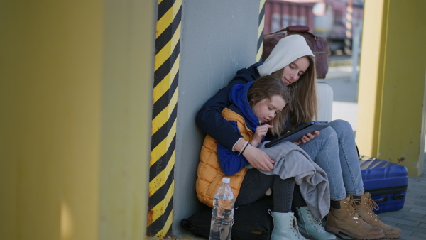 An Ukrainian immigrants sitting and waiting at railway station, using tablet.