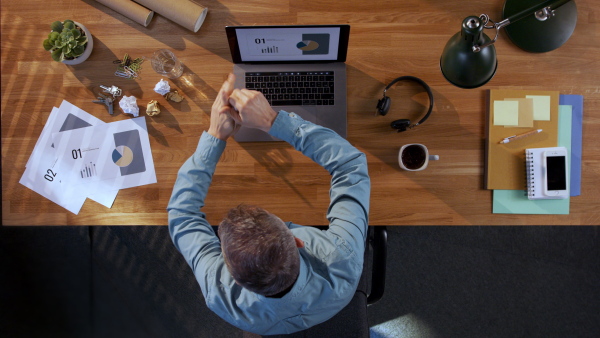A top view of businessman working on computer at desk in home office, getting angry.