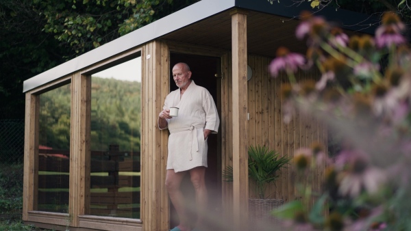 Handsome older man relaxing after spa session in home sauna, drinking herbal tea. Concept of hygge and slow life for senior people.