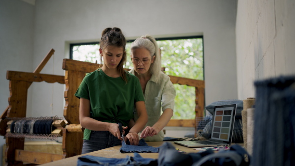 Mom teaching her daughter how to prepare material for weaving. Working together in family workshop. Sustainable business, using recycled materials in fashion.