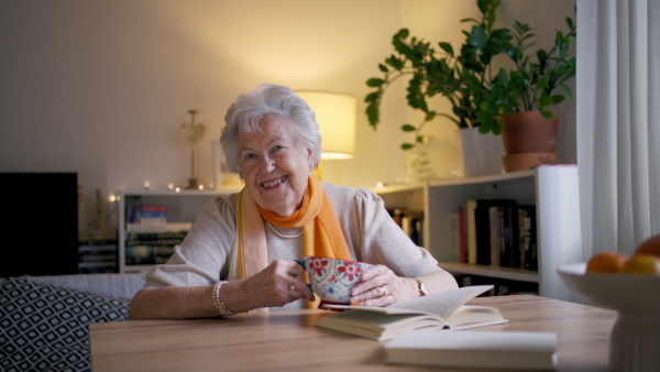 Lovely elderly woman sitting at the kitchen table and drinking a tea. Video of senior woman at home.