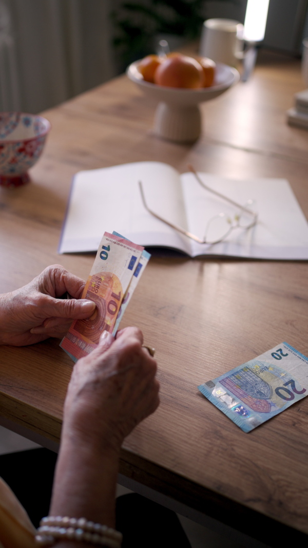 Close up of elderly woman looking sadly at few banknotes in her hand. Concept of financial struggles for seniors.