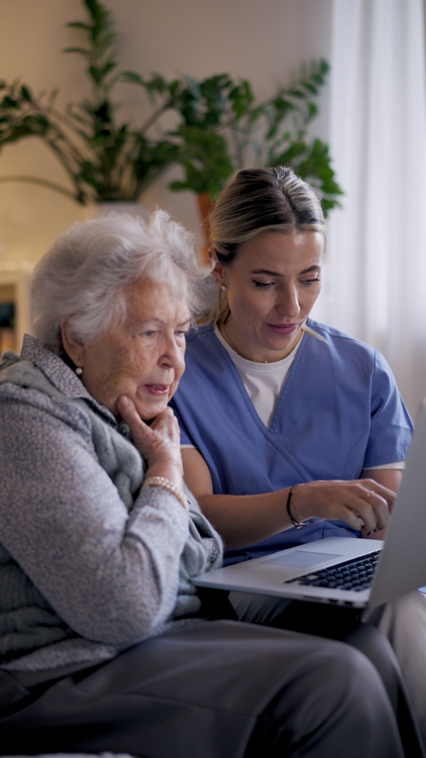Social worker helping elderly lady with managing her finances and teaching her to use laptop.