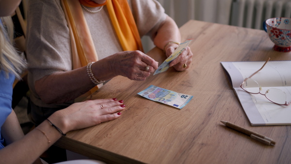 Close up of elderly woman looking sadly at few banknotes in her hand. Concept of financial struggles for seniors.