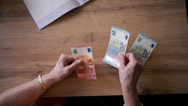 Close up of elderly woman looking sadly at few banknotes in her hand. Concept of financial struggles for seniors.
