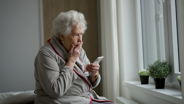 A horrified senior woman scrolling her smartphone. Phone scams on elderly people.