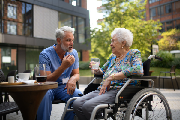Male nurse having a cup of coffee with senior patient in a wheelchair at a cafe.