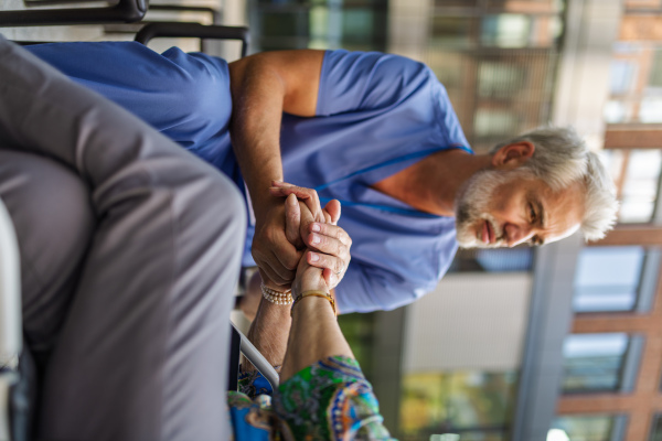 Close up of holding hands of male healthcare worker and senior patient.