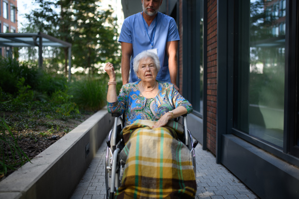 Male caregiver pushing senior woman in a wheelchair.