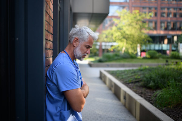 Frustrated and burnt-out doctor standing outside the hospital, feeling down. Mental health problems.