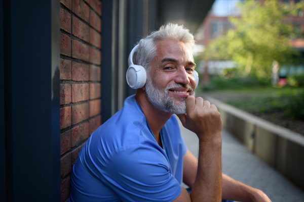 Healthcare worker relaxing with music outside hospital, headphones on head.
