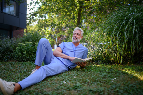 Healthcare worker resting in park outside hospital and reading book during break.